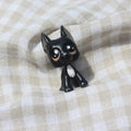 A small black great dane dog figurine with large white and brown eyes and a white chest patch, posed on a beige and white checkered fabric background.